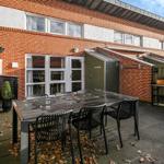 Terrace with table and chairs in front of brick house with windows and garden door.