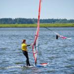 Windsurfer on water with red sail and another person in background.