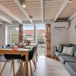 Living and dining area with sofa, table, and windows. Wooden ceiling and floral curtains.