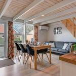 Living and dining area with sofa, table, and chairs. Wooden ceiling and windows with view outside.