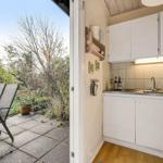 Kitchen with white cabinets and view of a paved balcony with chairs.