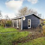 Black wooden house with garden and terrace. Satellite dish and windows visible.