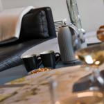 Black leather sofa with blanket, table with coffee mugs and kettle.
