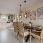 Dining room with table and chairs, kitchen area in background, wall art with Denmark motifs.