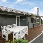 Terrace with white table and chairs in front of gray house with garden.