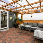 Terrace with seating group, table, and string lights under glass roof.