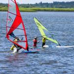 Two windsurfers practice on the water with colorful sails.