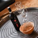 On a metal tray, a wine bottle, two glasses, and a bowl with pine nuts are placed.