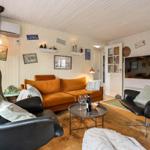 Living room with orange sofa, two black chairs, and TV mounted on the wall.