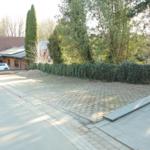 Pflasterter Hof mit Hecke und Wohnhaus im Hintergrund.