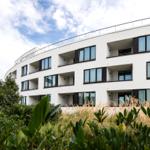 Modernes Mehrfamilienhaus mit Balkonen und grüner Umgebung.