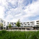 Moderne Wohngebäude mit Balkonen und Parkplätzen unter blauem Himmel.