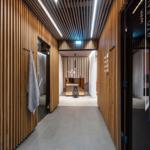 Holzgetäfelte Flure mit Tür zu Bio-Sauna und Ruheraum. Zentraler Tisch mit Blumen.