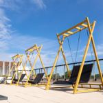 Drei gelbe Schaukelstühle auf einer Terrasse mit blauem Himmel.