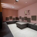 Raum mit Sitzbänken an rosa Wänden und geometrischem Wandbild.