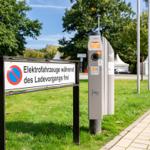 Ladestation für Elektrofahrzeuge mit Schild auf Grünfläche neben Gehweg