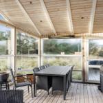 Patio with table and chairs, large windows and wooden ceiling.