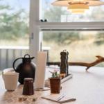 Dining table with tablecloth, coffee pot, notebook, and dice by window.