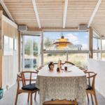 Dining room with table, chairs, and large windows. Wooden ceiling and white wall.