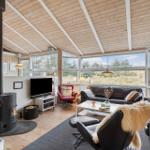 Living room with wooden ceiling, large windows, and black leather furniture.