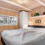 Bedroom with wooden walls, bed, and window. Shelf with items above the headboard.