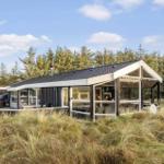 Modern cabin with large glass area, terrace, and hot tub in grassland with forest in background.