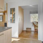 Kitchen with wooden cabinets and view into living area with chair and window.