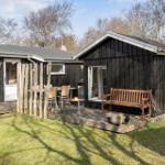 Black wooden house with terrace, bench, and fire pit in the garden.