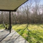 Deck with wooden roof and view of green lawn and trees.