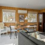 Living room with dining table, sofa, and wood stove. Wooden walls and large windows.