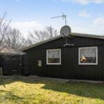 Black wooden house with satellite dish and two windows. Lawn and trees in the background.