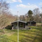 Two wooden houses with terraces stand in a green garden surrounded by trees.