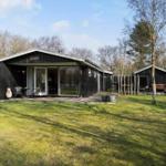 Black wooden cabin with terrace and garden. Attached building with fire pit.