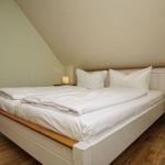 Schlafzimmer mit Doppelbett, Nachttischen und Holzboden unter schräger Decke.