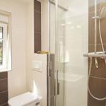 Bad mit Dusche, Toilette und Fenster. Fliesen in Beige und Braun.