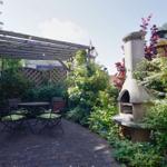 Garten mit Sitzgruppe, Pergola und Steinofen umgeben von Pflanzen.