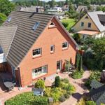Rotes Backsteingebäude mit Balkon und Garten. Umgeben von Bäumen und Nachbarhäusern.