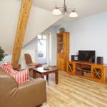 Wohnzimmer mit Sofa, Holzmöbeln und TV. Holzdecke und Fenster sichtbar.