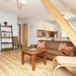 Wohn- und Küchenbereich mit Sofa, Tisch und Holzboden unter Dachschräge.