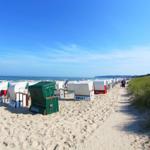 Strand mit Liegestühlen und sandigem Pfad zur See.