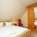 Schlafzimmer mit Doppelbett, Holzschrank und roter Sitzgelegenheit.