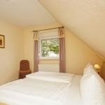 Schlafzimmer mit Dachschräge, Bett, Fenster und Stuhl.