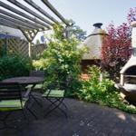 Terrasse mit Tisch, Stühlen und Grillofen im Garten.