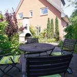 Garten mit Holztisch, Stühlen und Grill. Umgeben von Bäumen und Sträuchern.