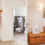 Schlafzimmer mit Kleiderschrank, Holzkommode und Blick in die Toilette.