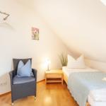 Ein Schlafzimmer mit Dachschrägen, Bett, Nachttisch, Stuhl und Kleiderständer.