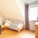 Ein Schlafzimmer mit Dachschrägen, Bett, TV und Fenster mit Vorhängen.