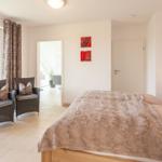 Schlafzimmer mit Bett, zwei Sesseln und Blick auf Balkon.