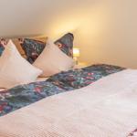 Das Bett ist mit einem floralen Bettbezug und Kissen bezogen. Eine Nachttischlampe steht daneben.