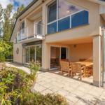 Haus mit Terrasse, Tisch und Stühlen, kleinem Teich und Balkon im Hintergrund.